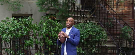 Tiki Barber holding football wearing a blazer