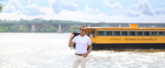 man in white t-shirt holding a blazer in front of water