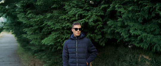 man in navy puffer jacket standing in front of lush trees