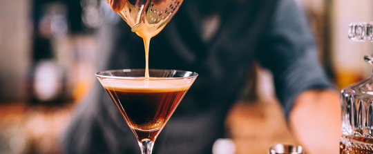 bartender pouring a cocktail into a martini glass