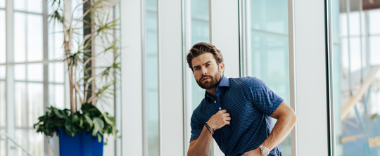 sharp dressed man in a polo sitting on a bench in front of glass windows